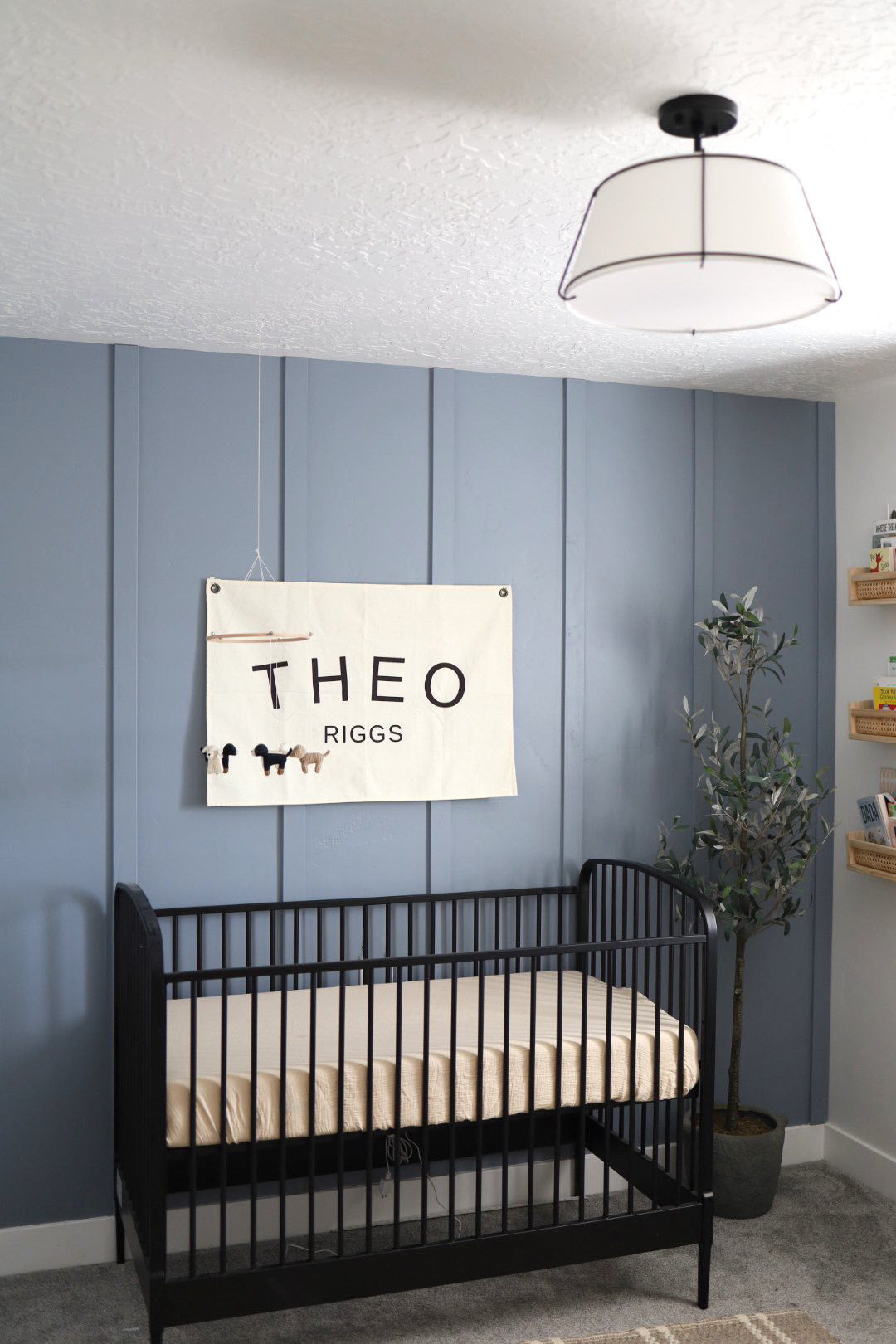 Custom canvas baby name banner with the name Theo Riggs hanging above black crib in nursery