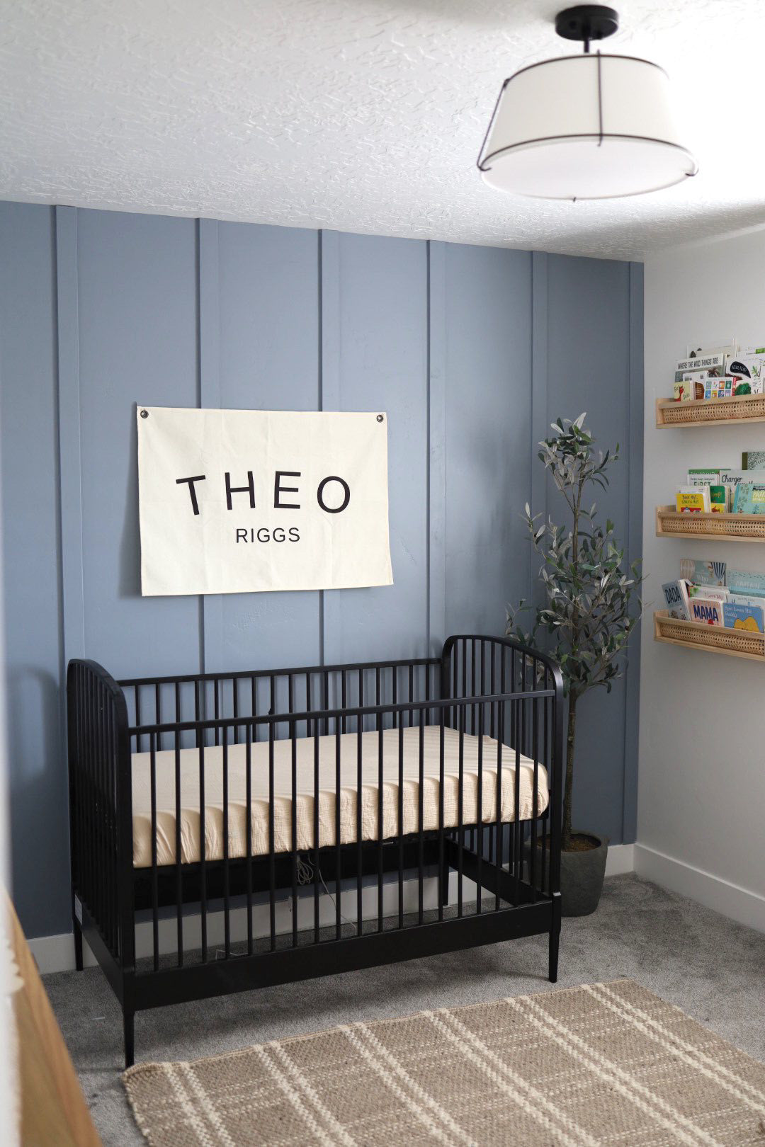 Custom canvas baby name banner with black letters hanging above black crib in modern nursery