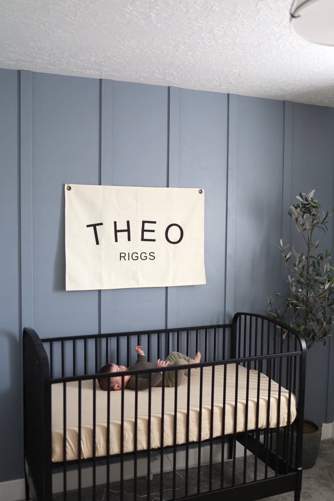Custom canvas baby name banner with Theo Riggs hanging above black crib in nursery room