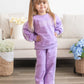 Young girl in a purple outfit standing in a living room with flowers and a couch.