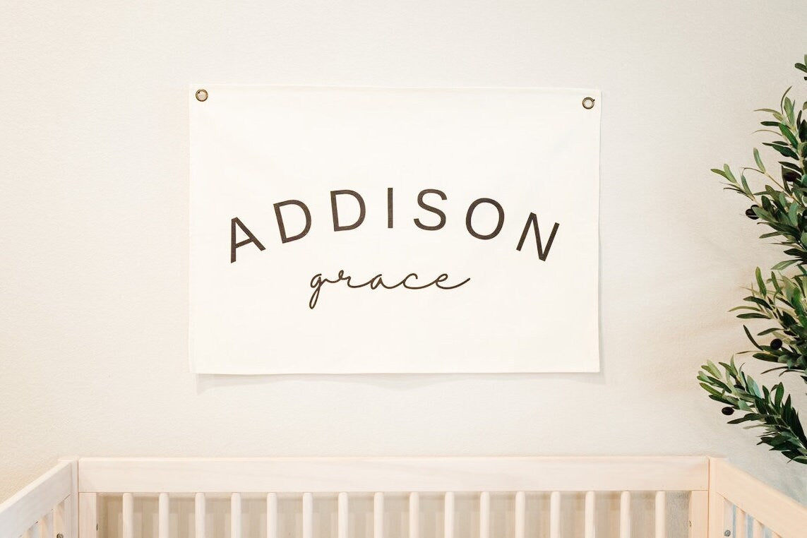 Custom canvas baby name banner with Addison Grace text hanging above wooden crib as nursery decor