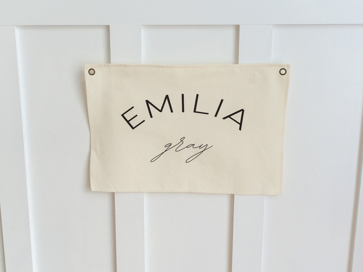 Custom canvas baby name banner by Little Joy Co. with the name Emilia Gray in black text on a cream canvas