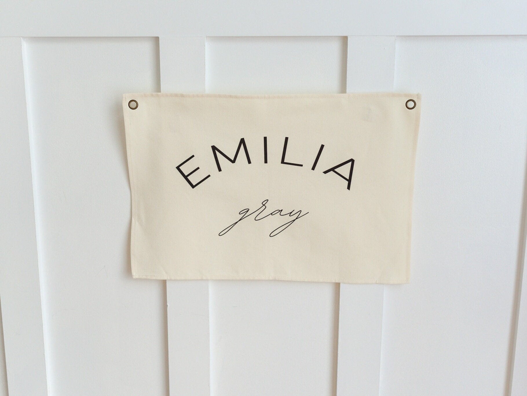Custom canvas baby name banner by Little Joy Co. with the name Emilia Gray in black text on a cream canvas