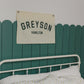 Custom canvas baby name banner with GREYSON HAMILTON hanging above white bed with star-patterned bedding and panda toy