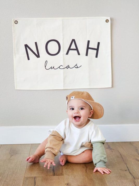 Custom canvas baby name banner with the name Noah Lucas hanging on wall behind smiling baby