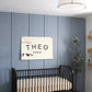 Custom canvas baby name banner with the name Theo Riggs hanging above black crib in nursery