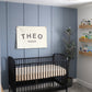 Custom canvas baby name banner with black letters hanging above black crib in modern nursery