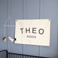 Custom canvas baby name banner with the name Theo Riggs hanging on a blue wall above a black crib