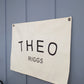 Custom canvas baby name banner with the name Theo Riggs printed in black letters on white canvas